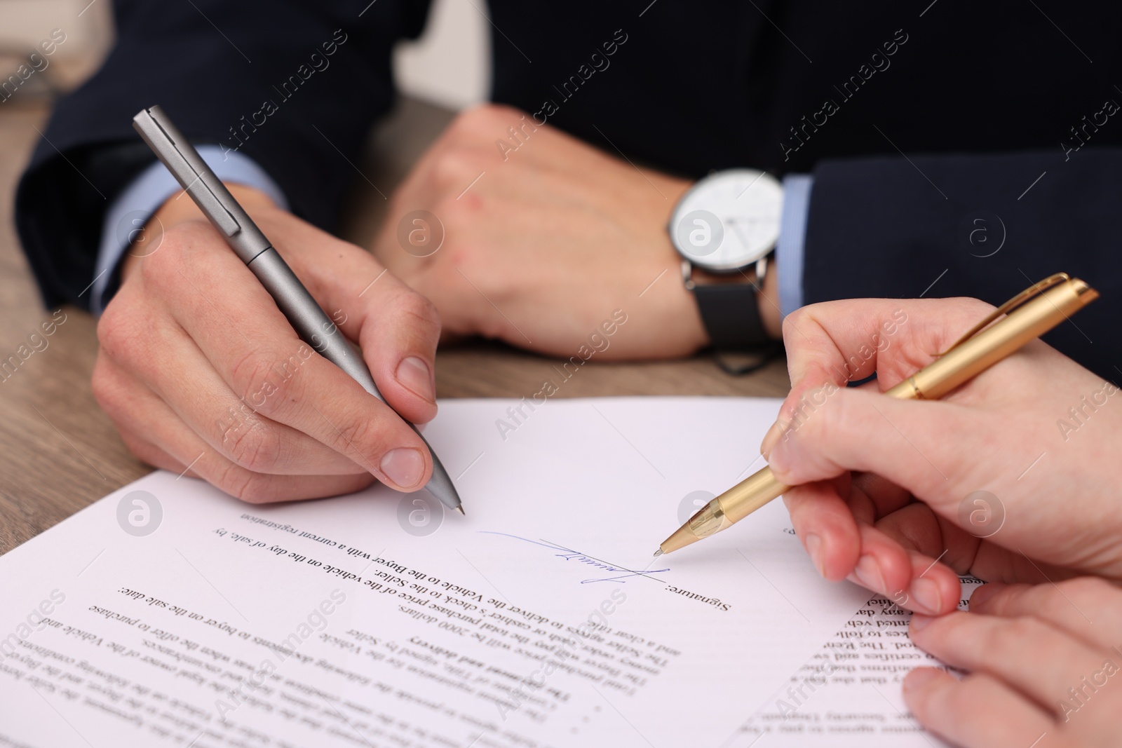 Photo of Woman pointing at document and man putting signature at table, closeup