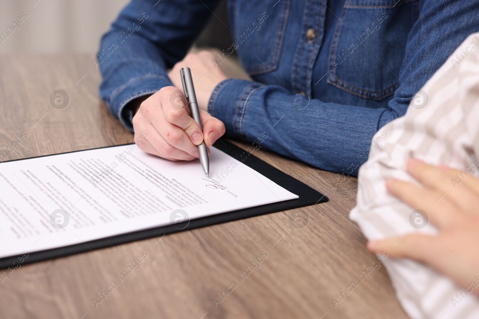 Photo of Woman putting signature on document at wooden table, closeup