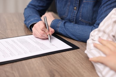 Photo of Woman putting signature on document at wooden table, closeup