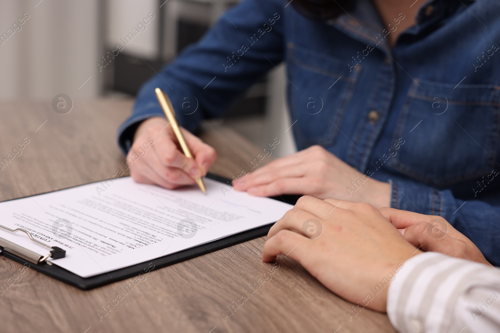 Photo of Woman putting signature on document at wooden table, closeup