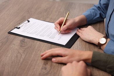 Photo of Woman putting signature on document at wooden table, closeup