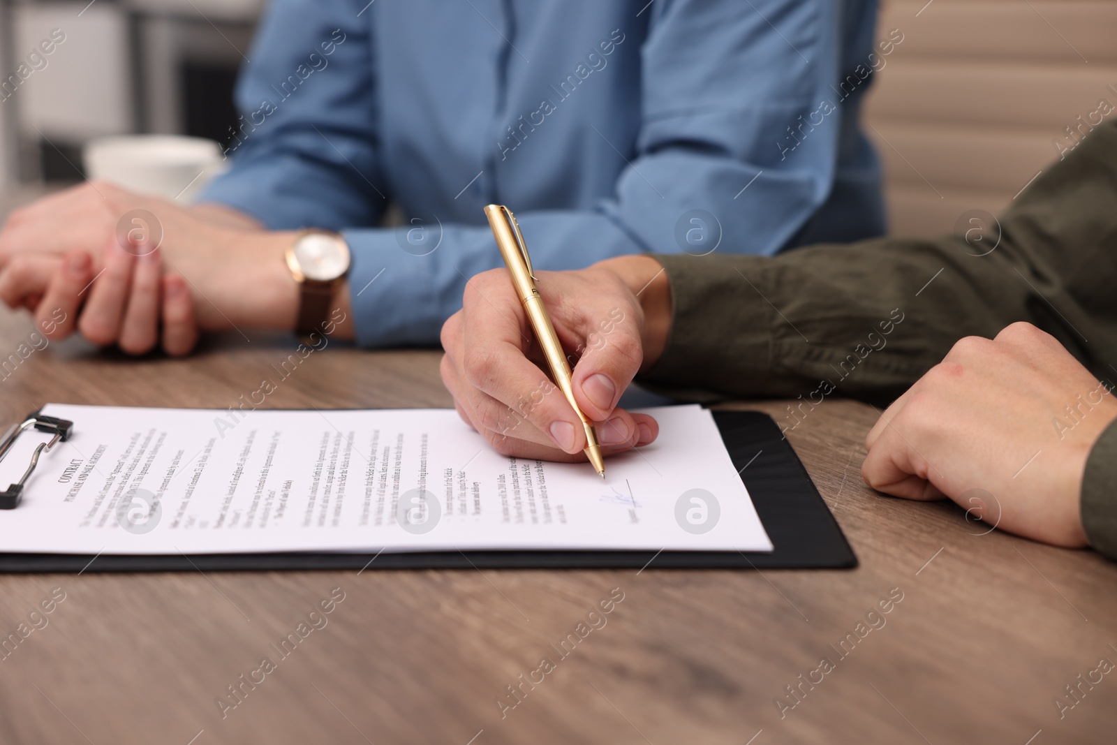 Photo of Man putting signature on document at wooden table, closeup