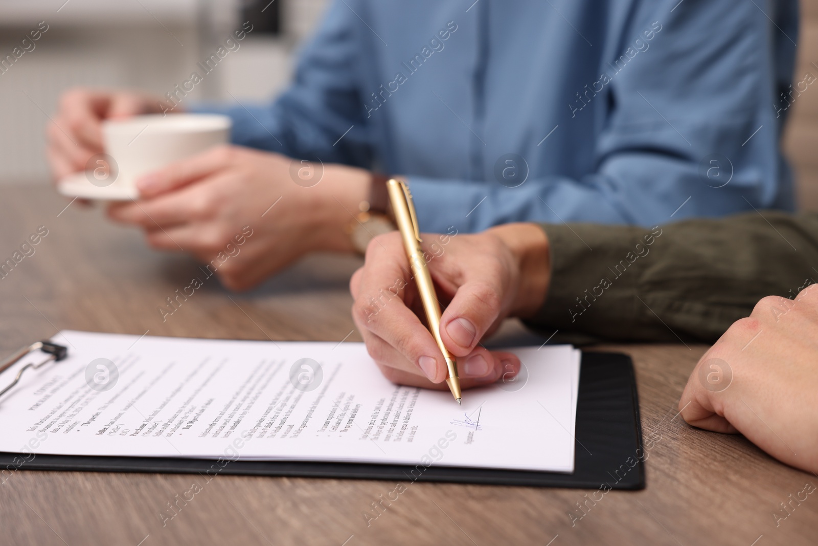 Photo of Man putting signature on document at wooden table, closeup