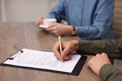 Photo of Man putting signature on document at wooden table, closeup