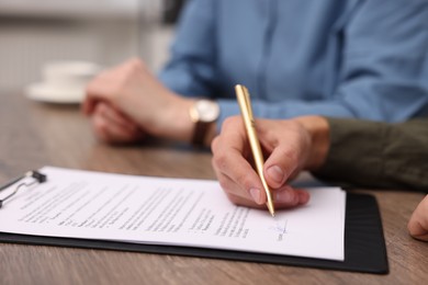 Photo of Man putting signature on document at wooden table, closeup