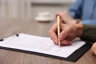 Photo of Man putting signature on document at wooden table, closeup