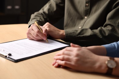 Photo of Man putting signature on document at wooden table, closeup