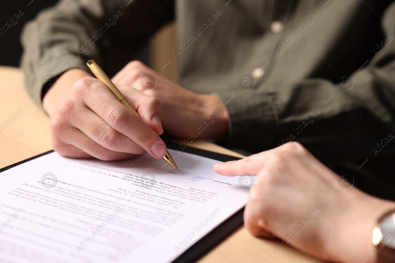 Photo of Woman pointing at document and man putting signature at table, closeup