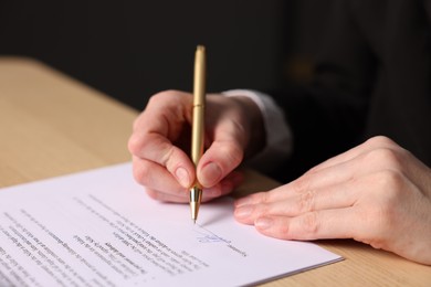 Photo of Woman putting signature on document at table, closeup