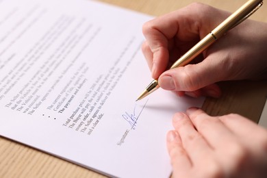 Photo of Woman putting signature on document at table, closeup