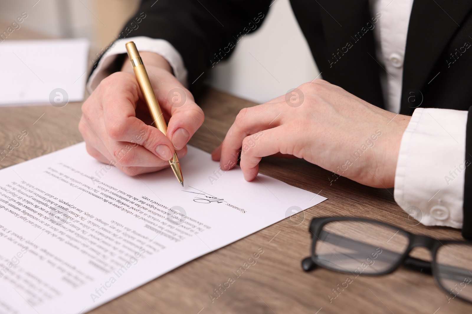 Photo of Woman putting signature on document at wooden table, closeup