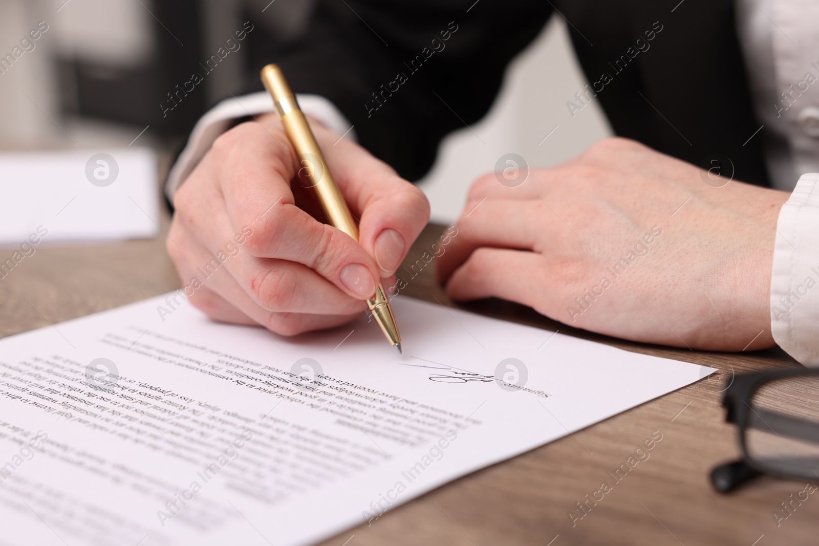 Photo of Woman putting signature on document at wooden table, closeup