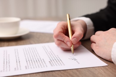 Photo of Woman putting signature on document at wooden table, closeup