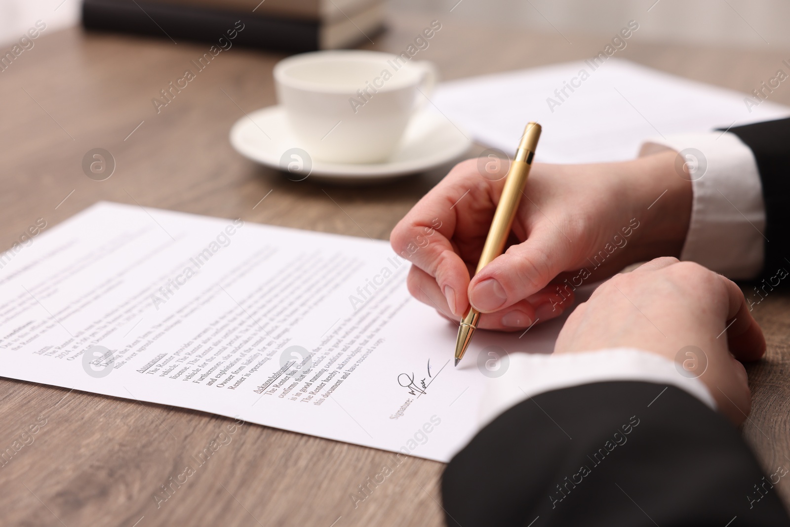 Photo of Woman putting signature on document at wooden table, closeup