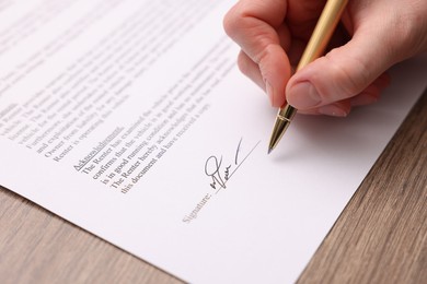 Photo of Woman putting signature on document at wooden table, closeup