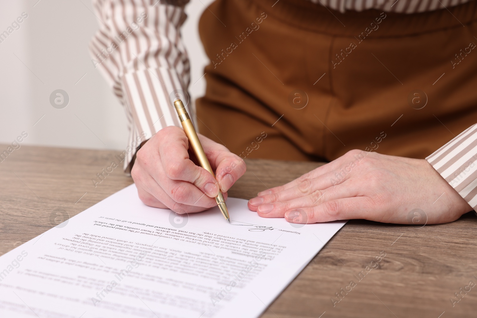 Photo of Woman putting signature on document at wooden table, closeup