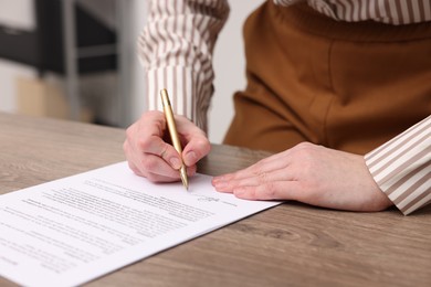 Photo of Woman putting signature on document at wooden table, closeup