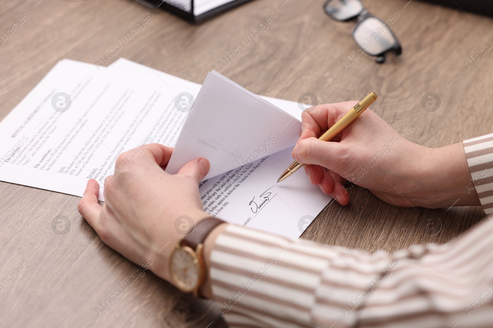 Photo of Woman putting signature on document at wooden table, closeup