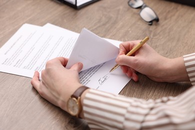 Photo of Woman putting signature on document at wooden table, closeup