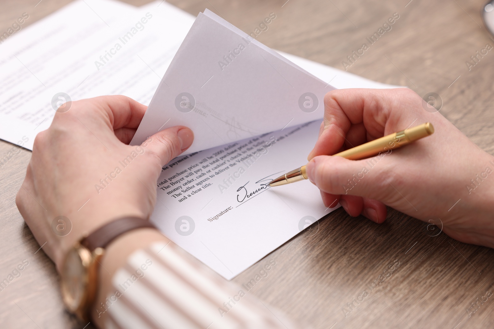 Photo of Woman putting signature on document at wooden table, closeup