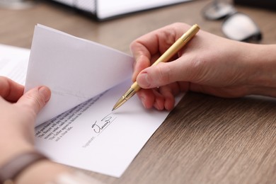 Photo of Woman putting signature on document at wooden table, closeup