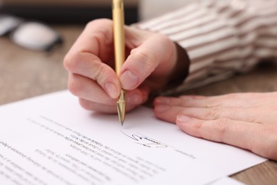 Photo of Woman putting signature on document at table, closeup