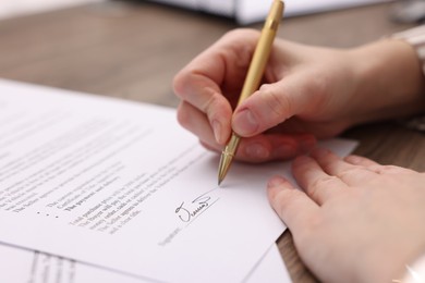 Photo of Woman putting signature on document at table, closeup