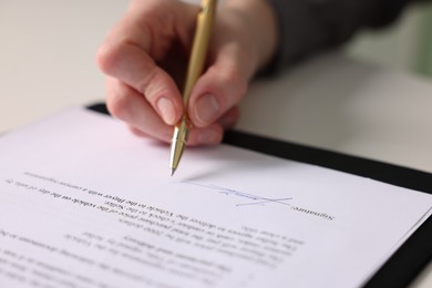 Photo of Woman putting signature on document at table, closeup