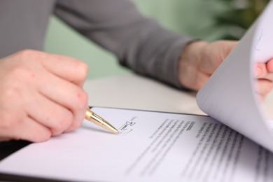 Photo of Woman putting signature on document at table, closeup