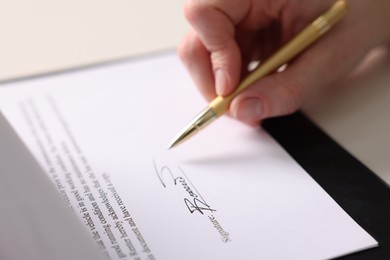 Photo of Woman putting signature on document at table, closeup