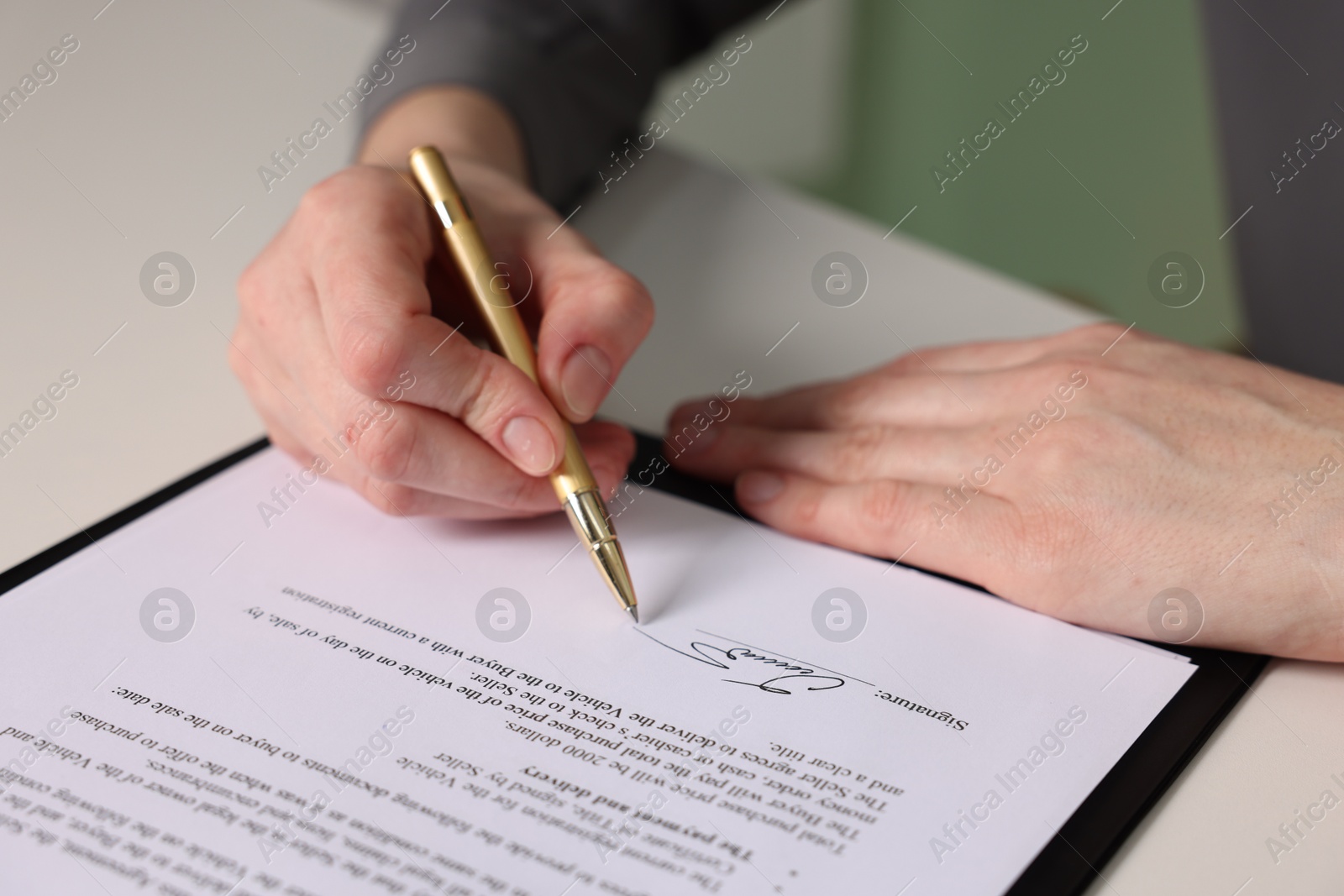 Photo of Woman putting signature on document at white table, closeup