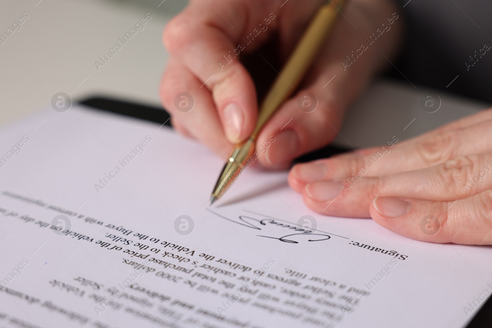 Photo of Woman putting signature on document at table, closeup