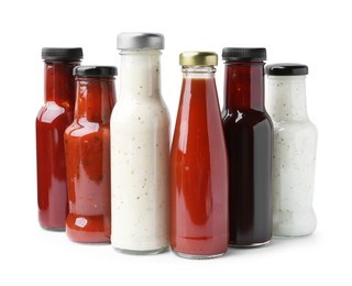 Photo of Different delicious sauces in glass bottles isolated on white