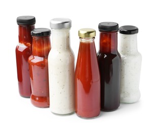 Photo of Different delicious sauces in glass bottles isolated on white