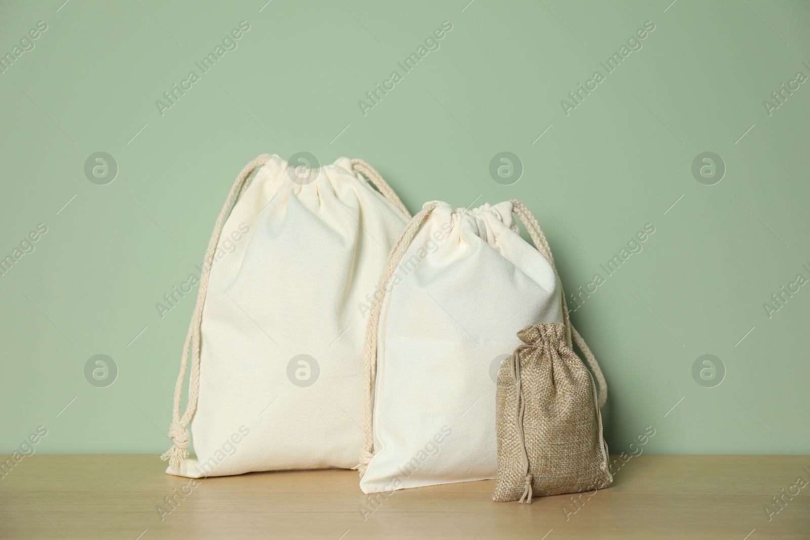 Photo of Burlap and cotton bags on wooden table against green background