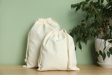 Photo of Cotton bags and houseplant on wooden table against green background