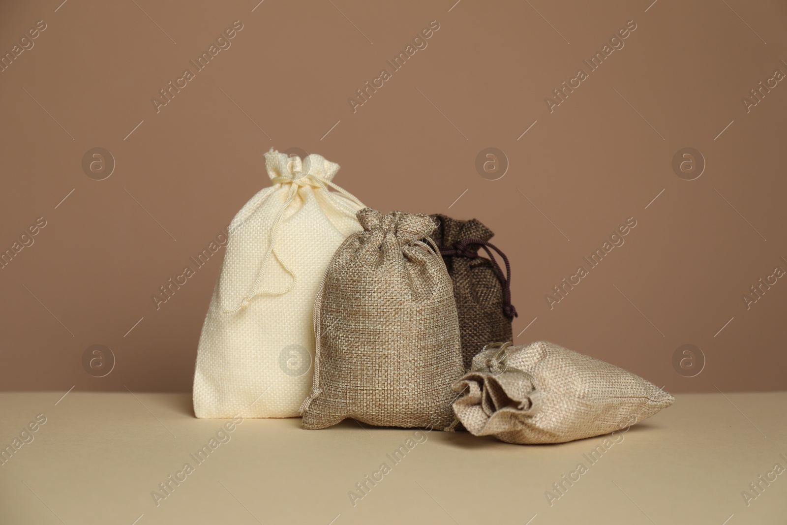 Photo of Different burlap bags on table against dark beige background