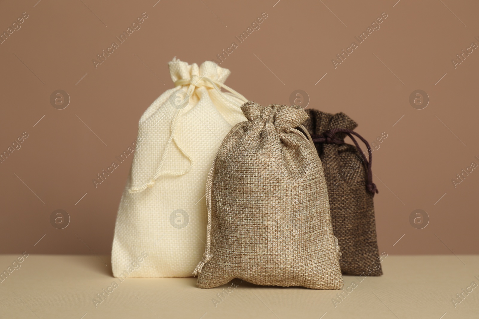 Photo of Different burlap bags on table against dark beige background