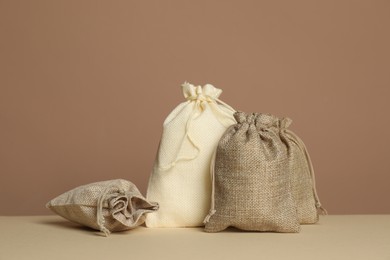 Photo of Different burlap bags on table against dark beige background