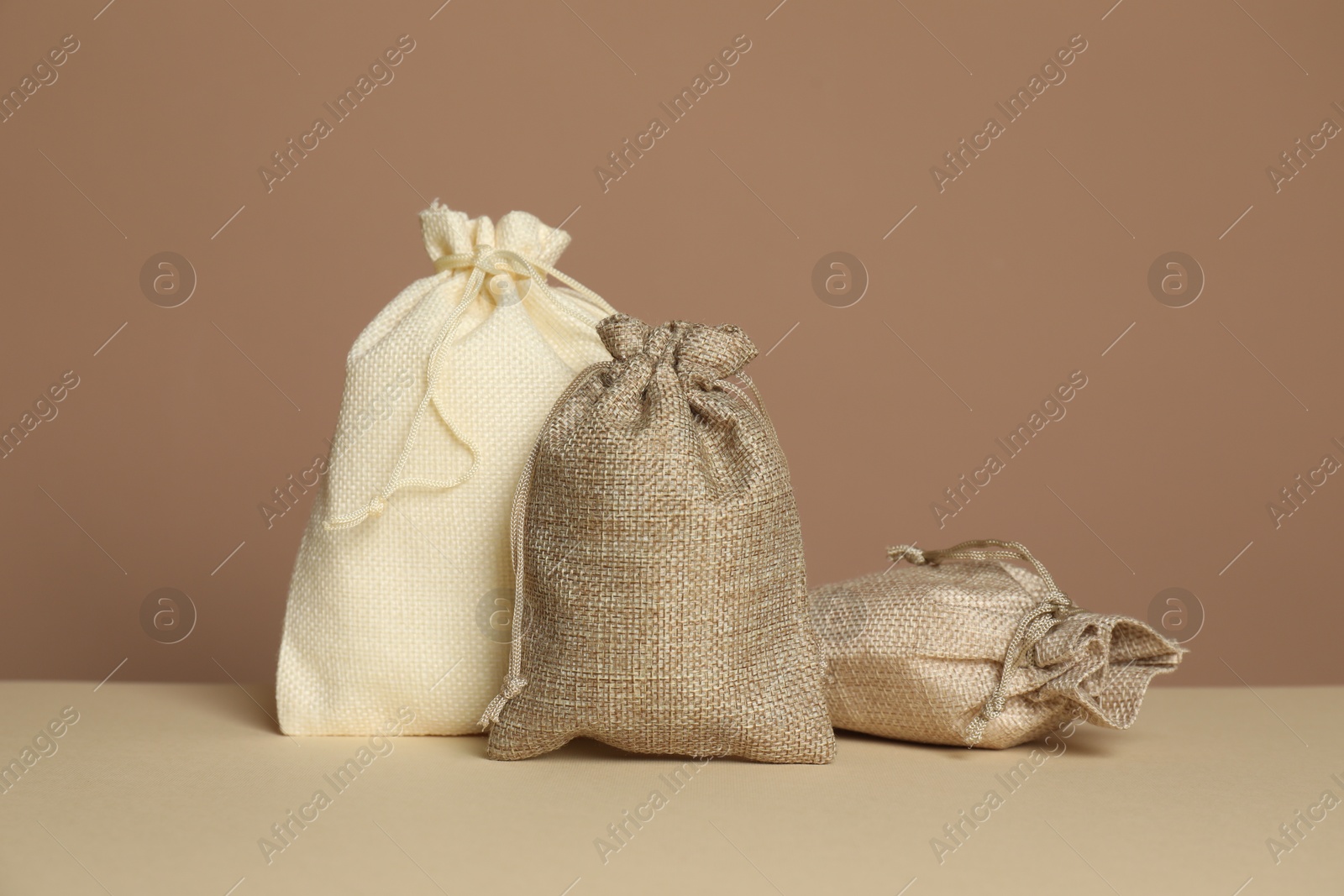 Photo of Different burlap bags on table against dark beige background