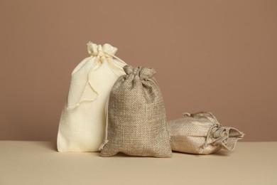 Photo of Different burlap bags on table against dark beige background