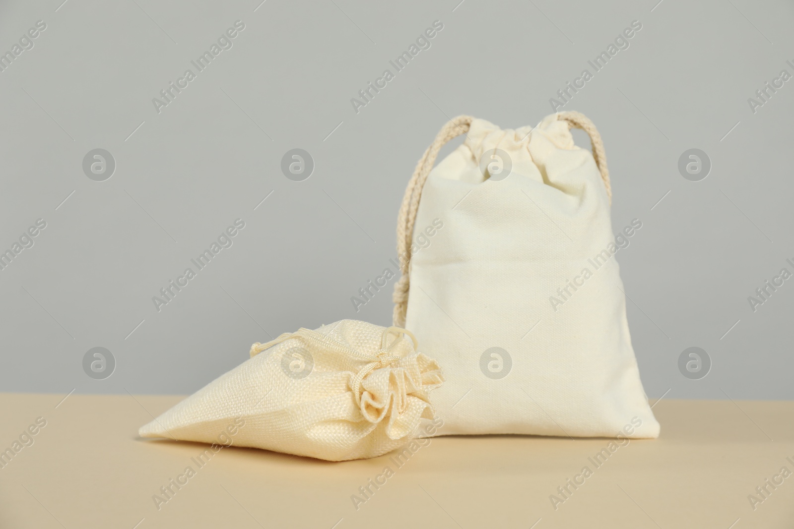 Photo of Burlap and cotton bags on beige table against grey background