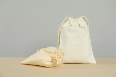 Photo of Burlap and cotton bags on beige table against grey background