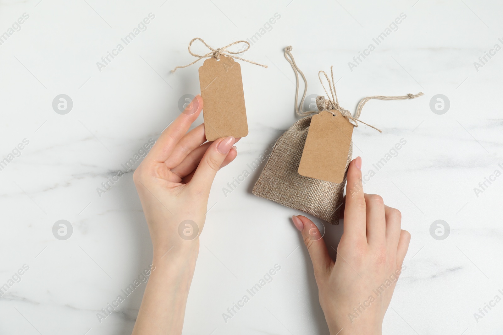 Photo of Woman with burlap bag and tags on white marble table, top view