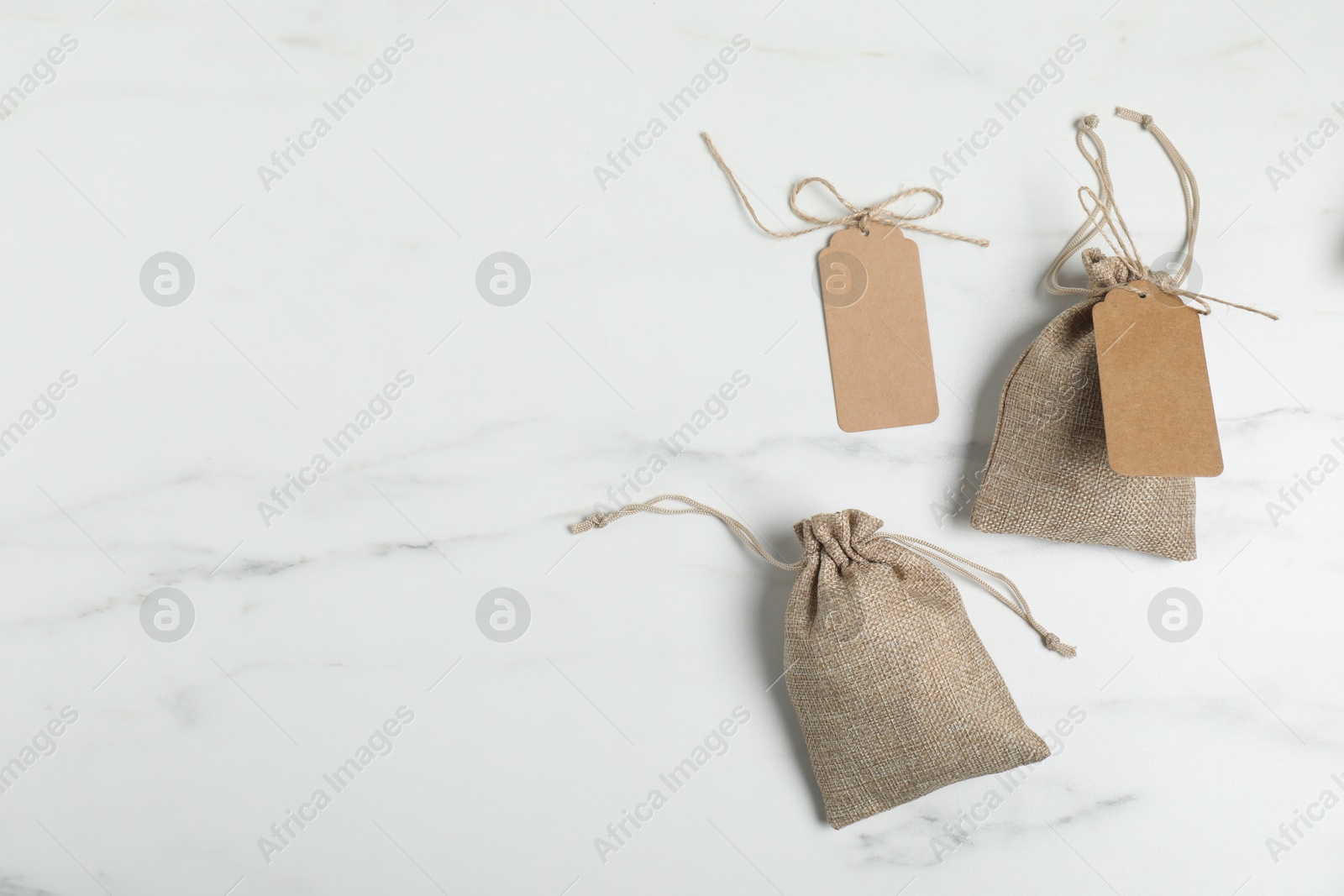 Photo of Burlap bags with tags on white marble table, flat lay. Space for text