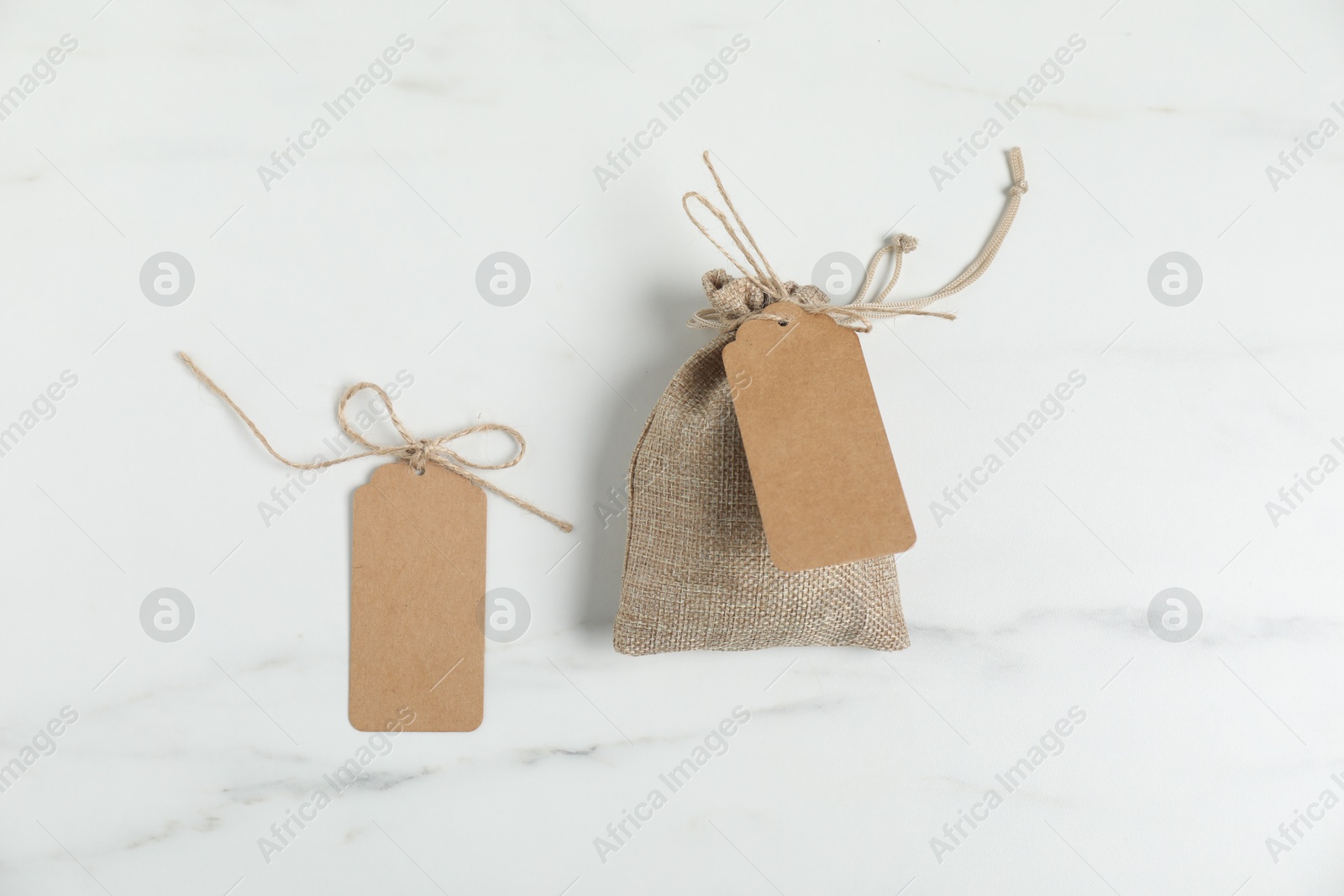 Photo of Burlap bag with tags on white marble table, flat lay