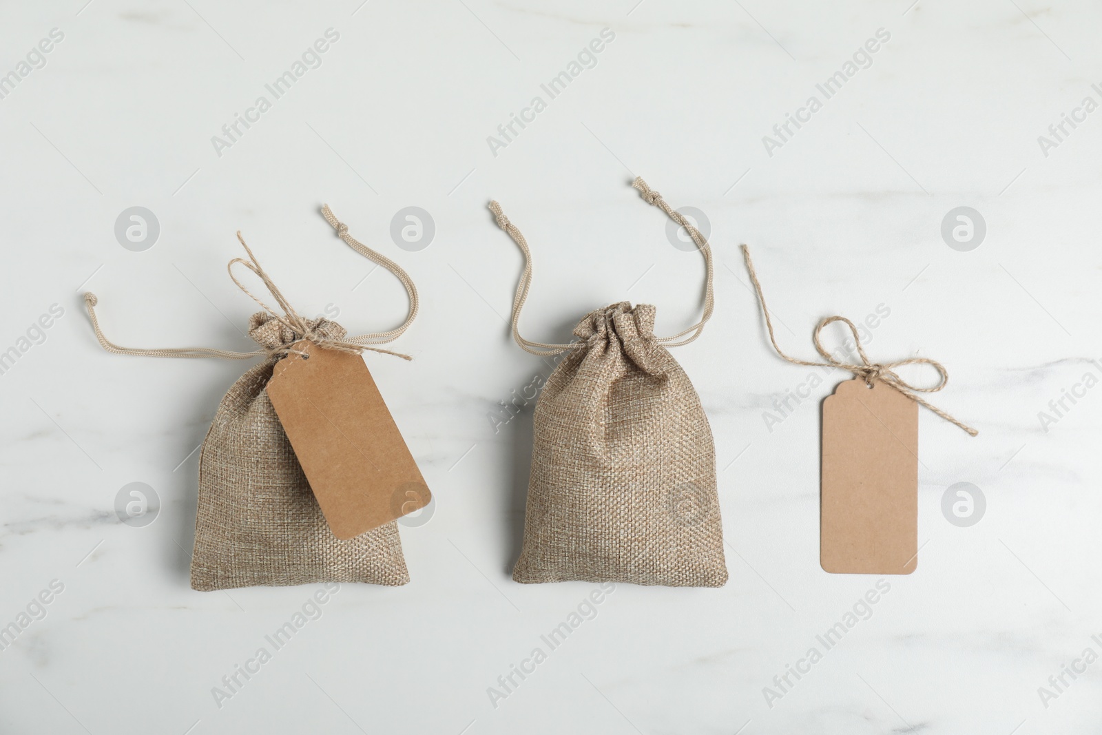 Photo of Burlap bags with tags on white marble table, flat lay