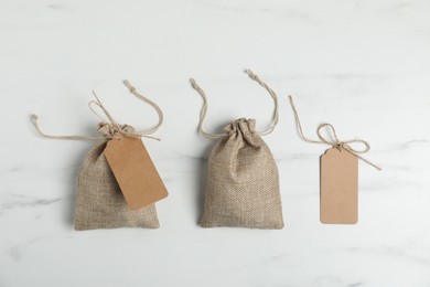 Photo of Burlap bags with tags on white marble table, flat lay