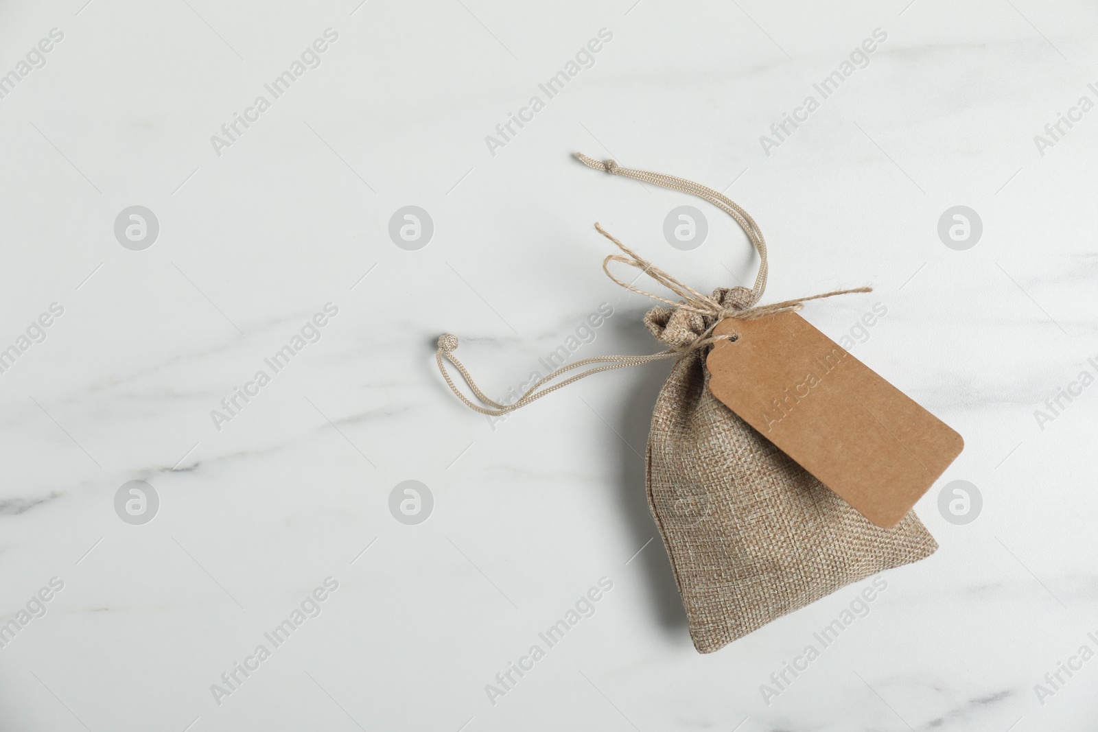 Photo of One burlap bag with tag on white marble table, top view. Space for text