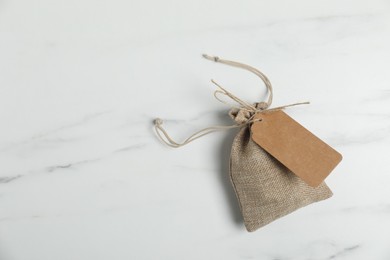 Photo of One burlap bag with tag on white marble table, top view. Space for text